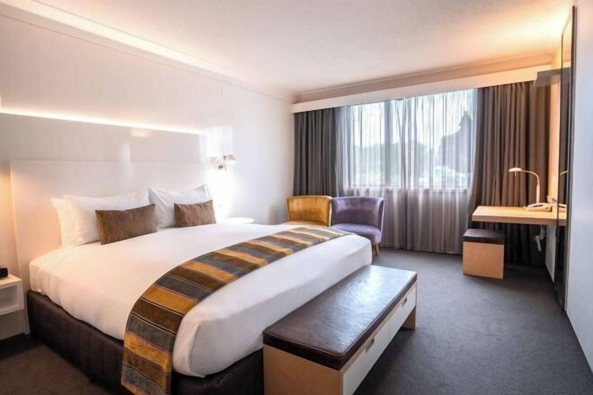 A hotel room with a large bed, a desk, a chair, and a window with curtains.