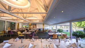 Un restaurant moderne doté de hauts plafonds, de grandes fenêtres et offrant différents types de sièges, notamment des tables et des banquettes.