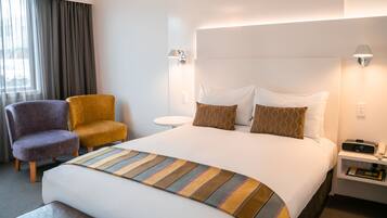 Une chambre d’hôtel avec un grand lit, deux chaises, une table de chevet, une lampe et une horloge.