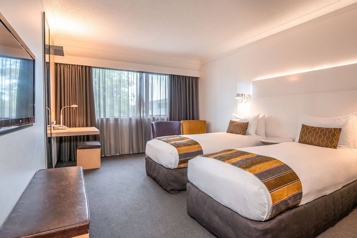 A hotel room with two beds, a desk, a chair, and a TV.