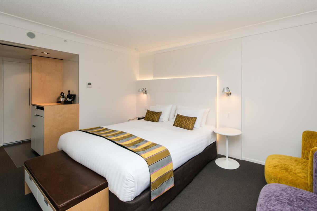 A hotel room with a bed, bedside table, chair, and a small white table.