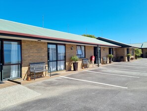 A motel with a parking lot, a covered outdoor seating area, and a brick facade.