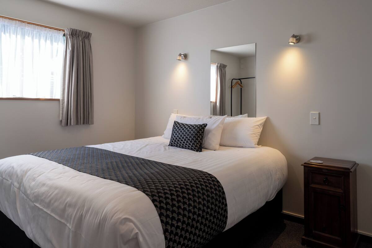 A neatly made bed with a patterned bedspread, a bedside table with a lamp, and a mirror on the wall.