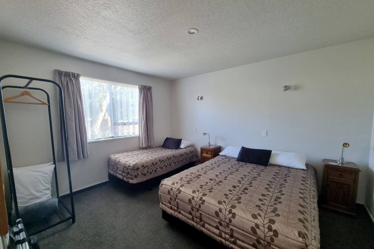 A room with two single beds, a bunk bed, a bedside table with a lamp, and a window with curtains.