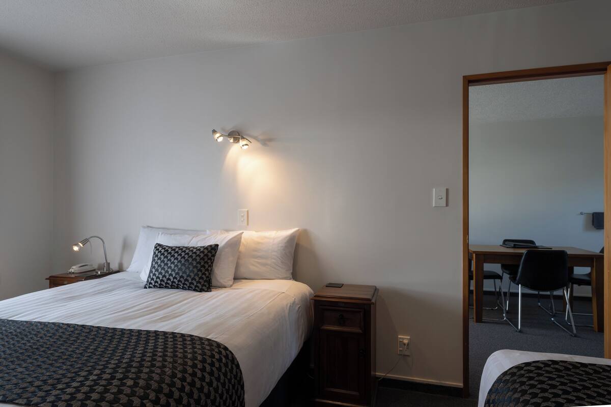 A hotel room with a bed, bedside tables, a desk with a chair, and a mirror.