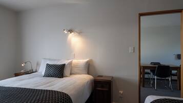 Una habitación de hotel con una cama, mesitas de noche, un escritorio con silla y un espejo.