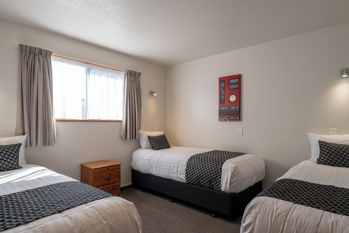 A hotel room with two single beds, a wooden nightstand, a wall-mounted light, and a window with curtains.
