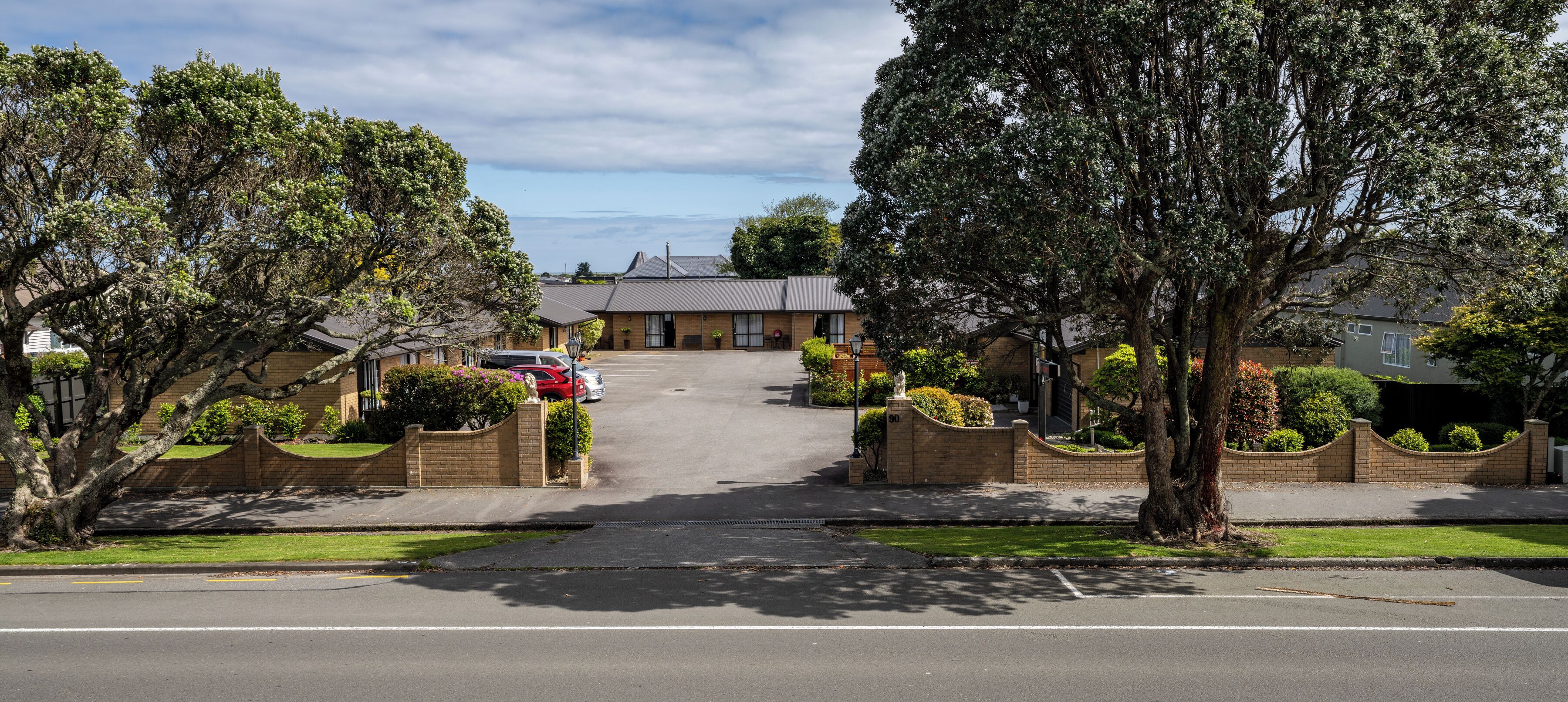 A residential street with houses, parked cars, and trees.