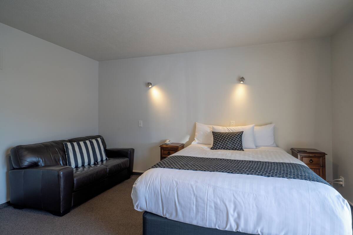 A bedroom with a large bed, a dark leather sofa, and two bedside tables.