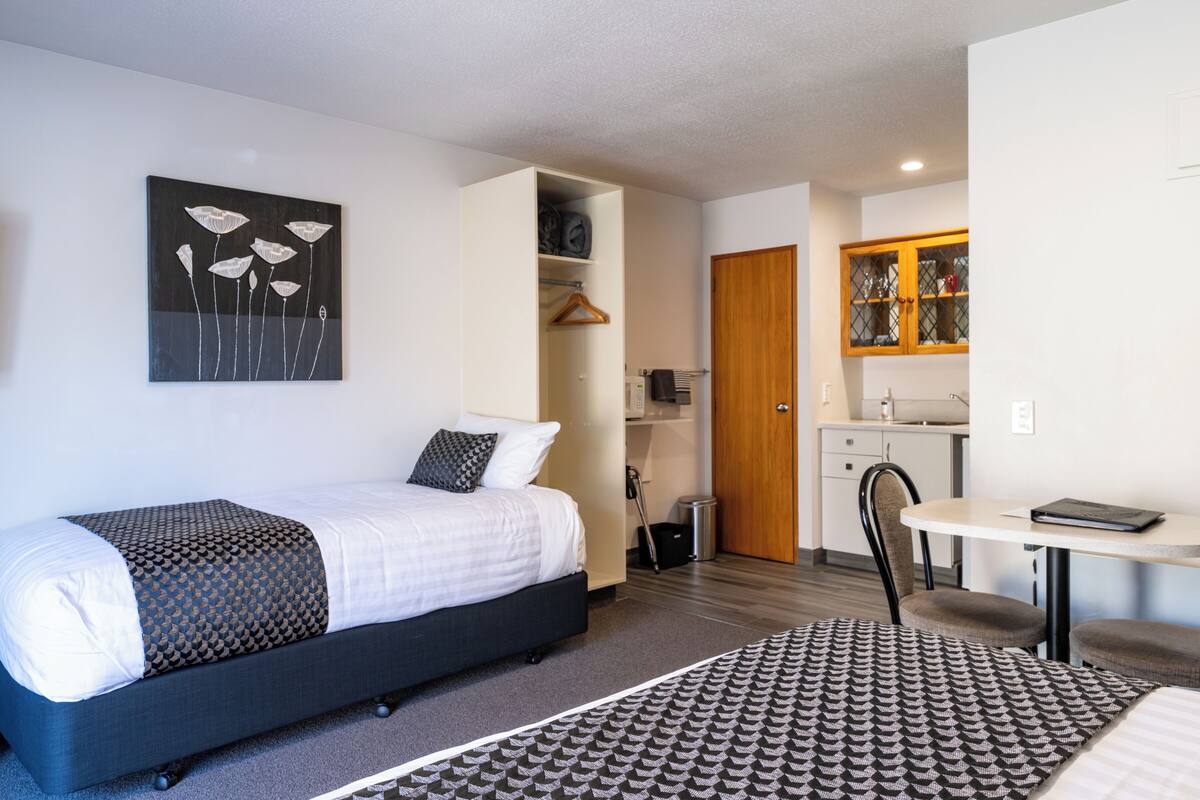 A modern hotel room with a bed, a desk, and a kitchenette.