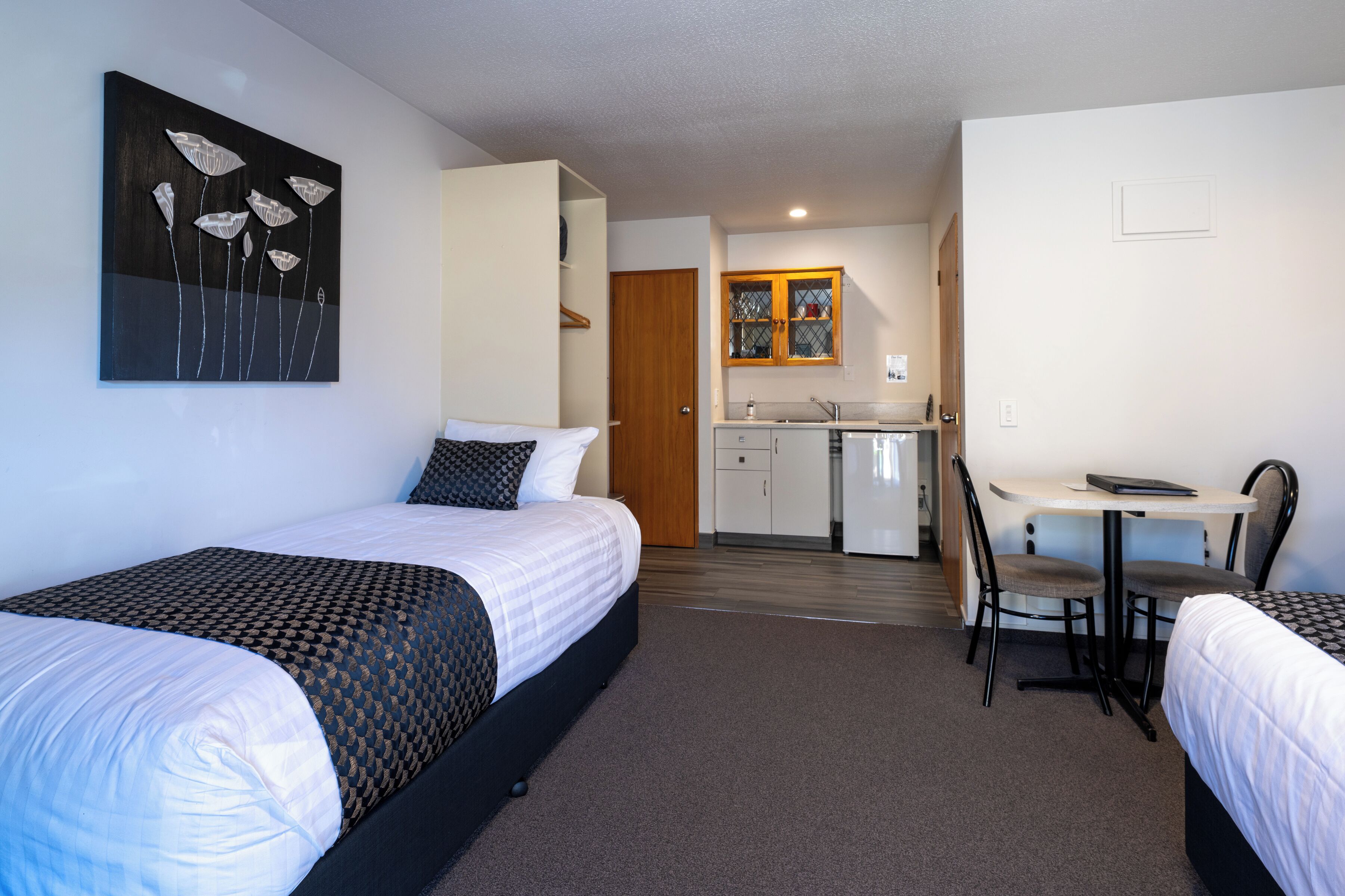 A hotel room with two beds, a desk, and a kitchenette.