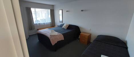 A bedroom with a bed, a bedside table, a dresser, a window with curtains, and a mirror on the wall.