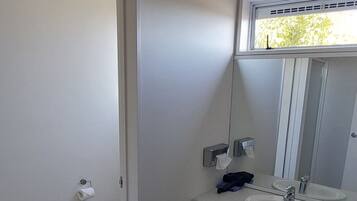 A bathroom with a toilet, sink, and mirror. There is a towel rack and a trash bin.