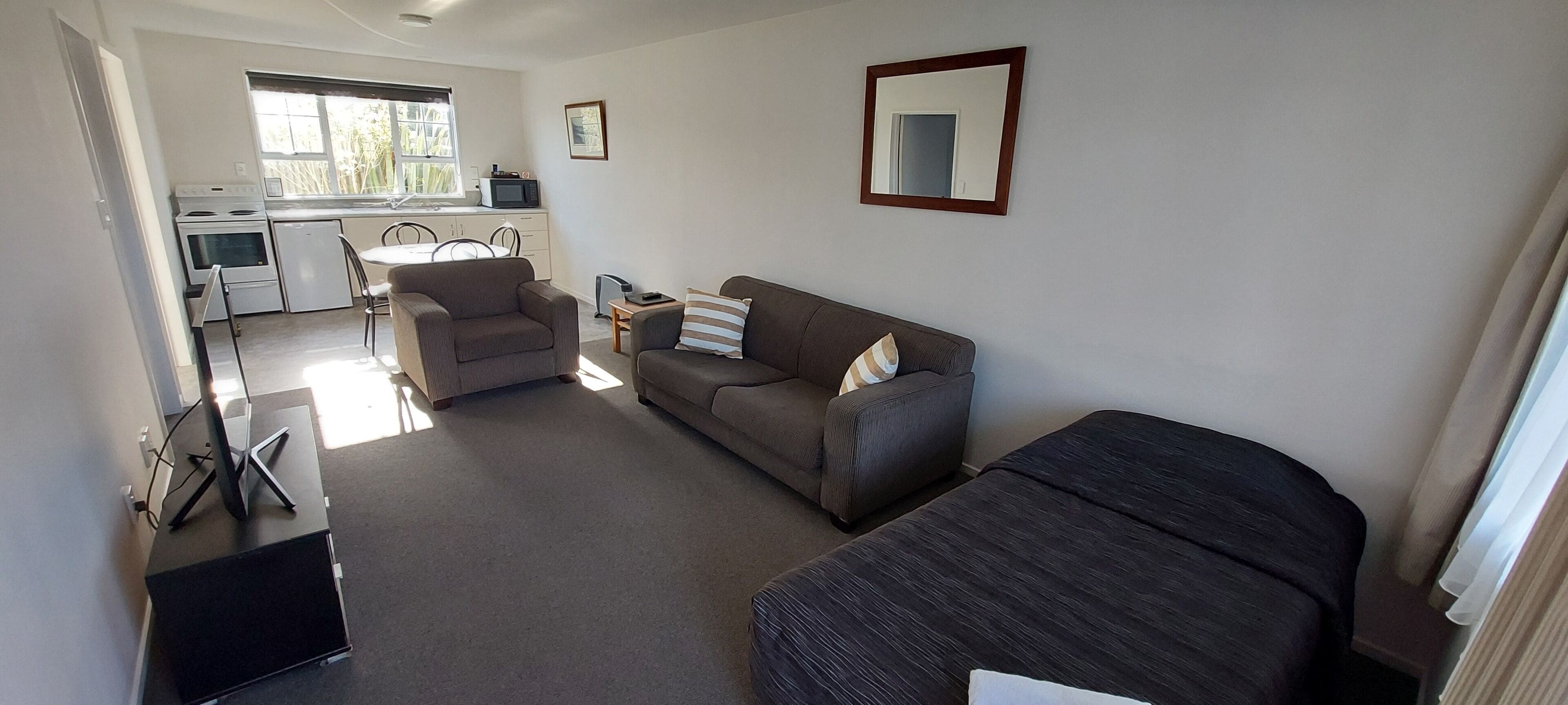 A compact living space with a kitchenette, a sofa, a chair, and a bed.
