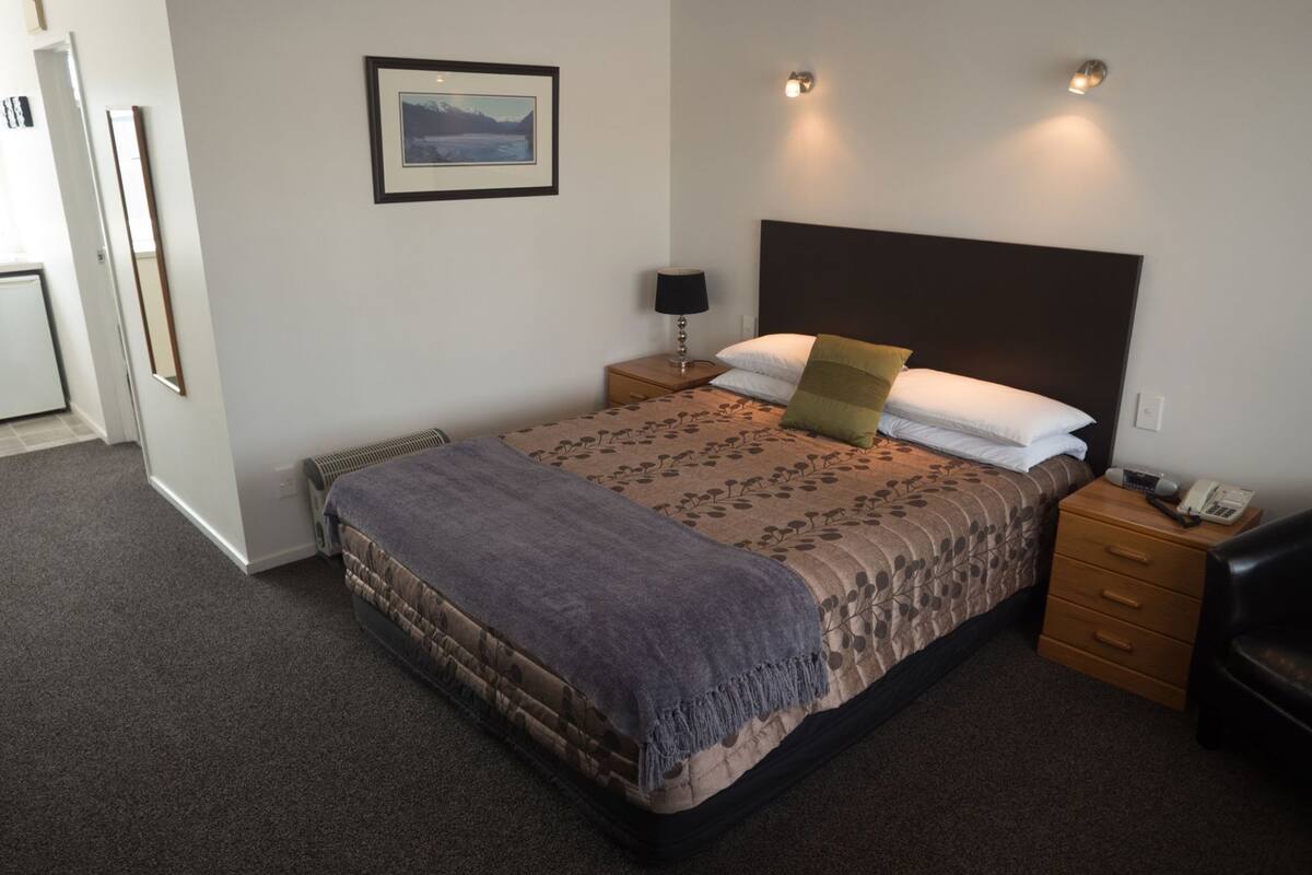 Quarto de hotel bem arrumado com uma cama, mesas de cabeceira, um abajur, um quadro na parede e um telefone na mesa de cabeceira.