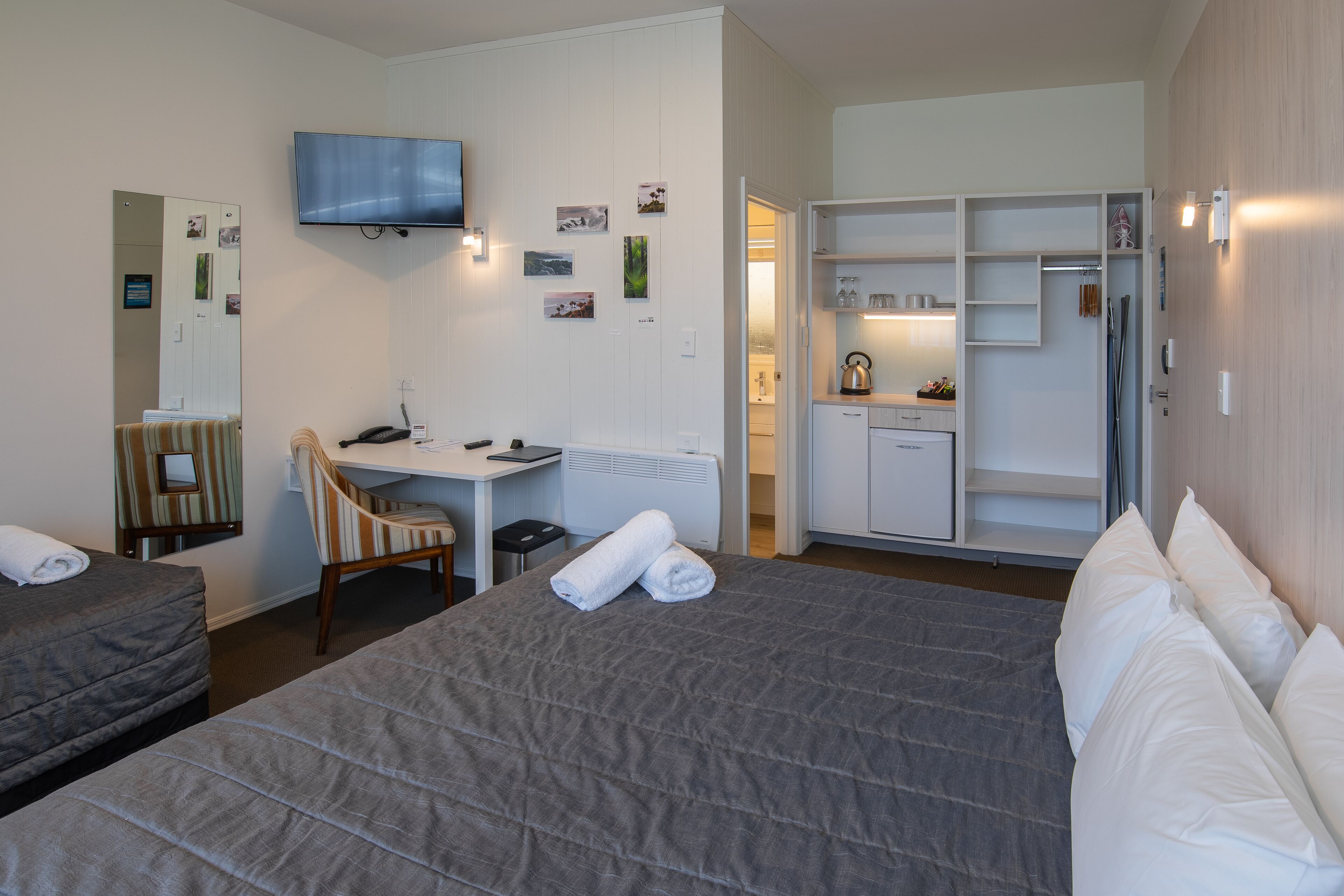 A hotel room with a bed, a desk, a chair, a TV, and a wardrobe.