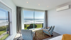 A modern room with large floor-to-ceiling windows offering a view of the ocean. There are two chairs and a small table in the room. - Beachfront Hotel (Hokitika)