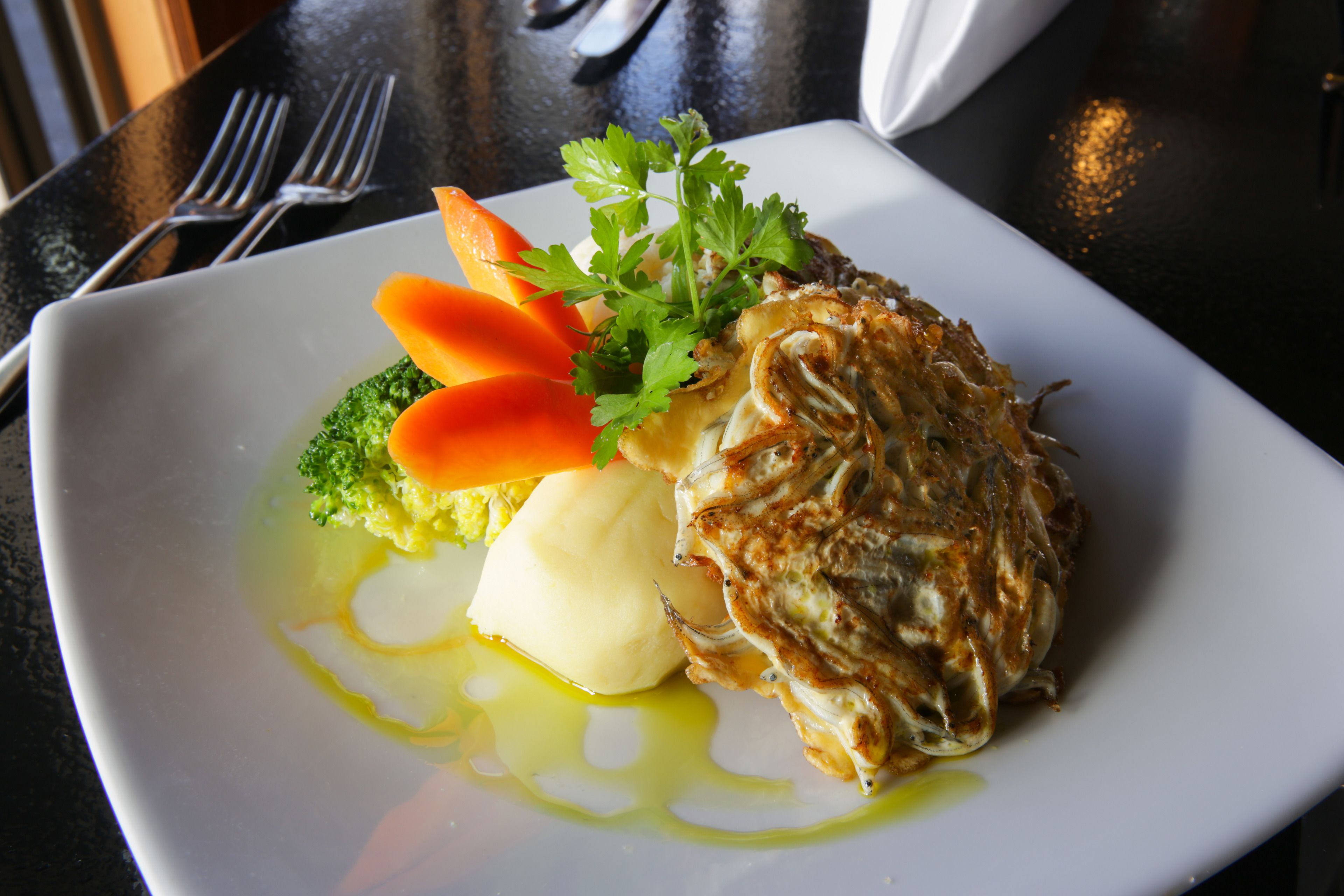 A square white plate with a piece of grilled chicken, broccoli, carrot slices, and a dollop of butter.
