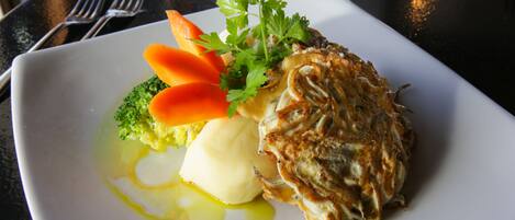 A square white plate with a piece of grilled chicken, broccoli, carrot slices, and a dollop of butter.