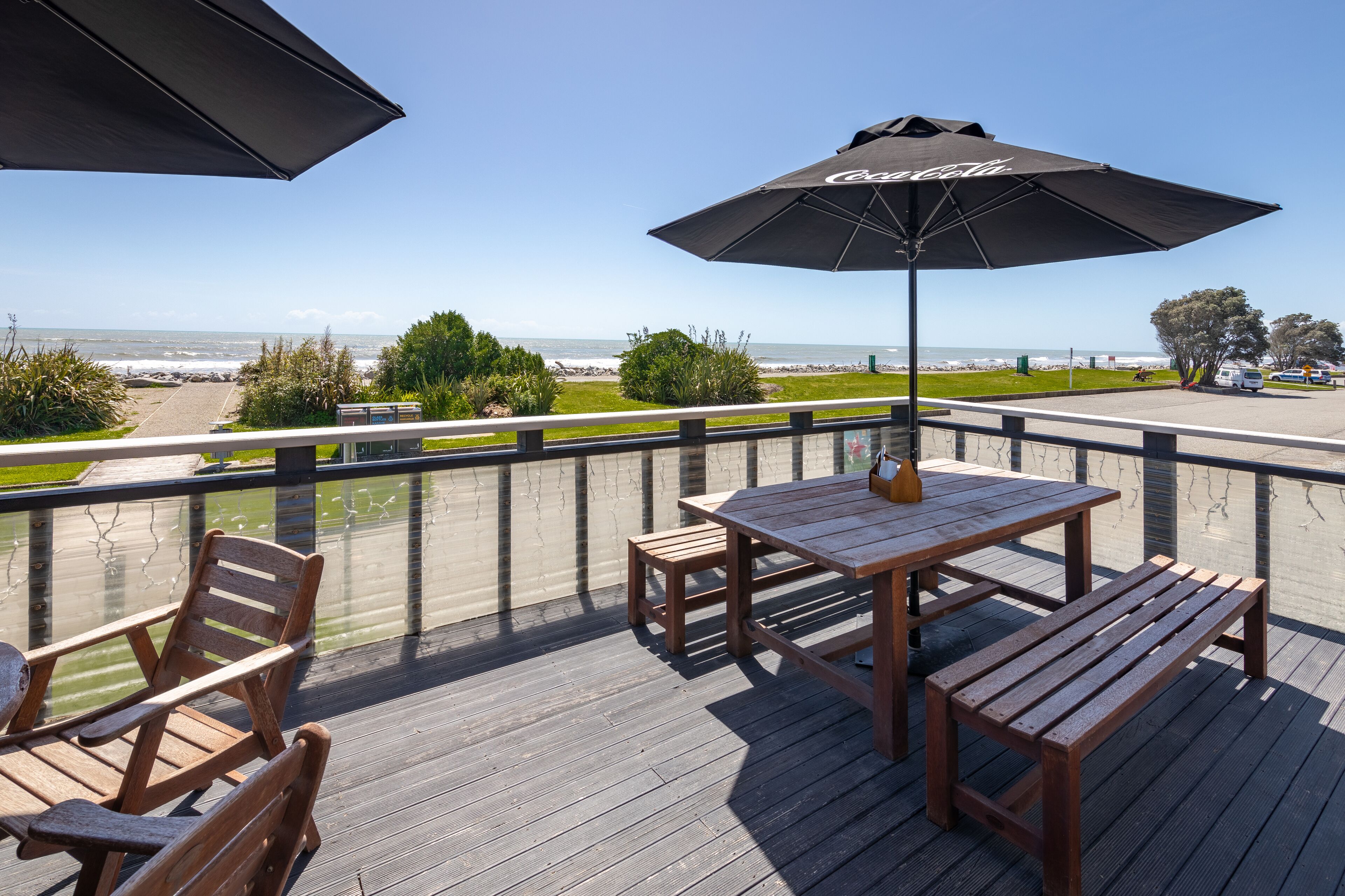 A wooden deck with a table and chairs, a black umbrella, and a view of the ocean.