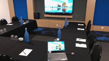 Un salón de conferencias con una pantalla grande, varias mesas con computadoras portátiles y botellas de agua.
