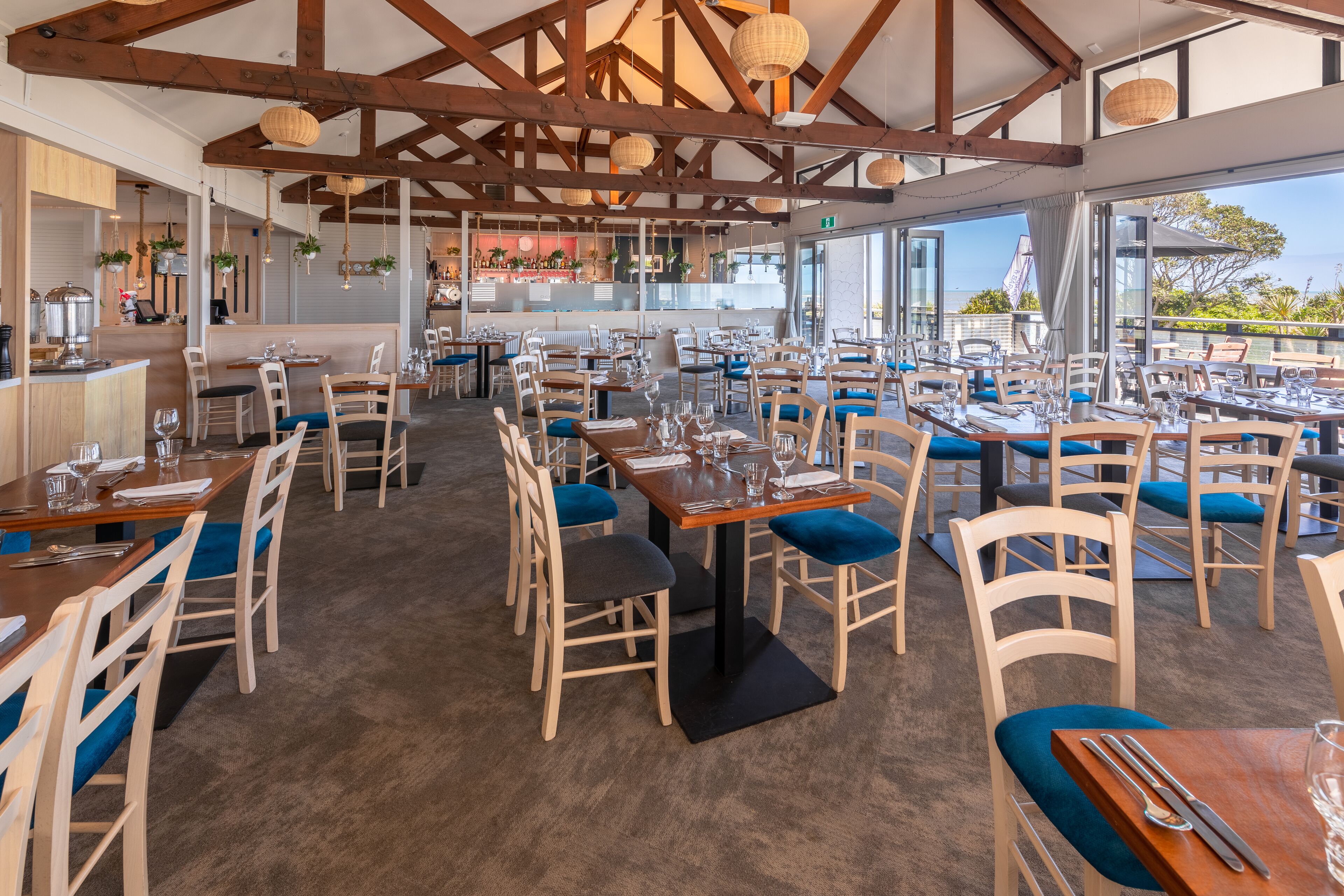 A restaurant with wooden tables and chairs, a bar area, and large windows offering a view.