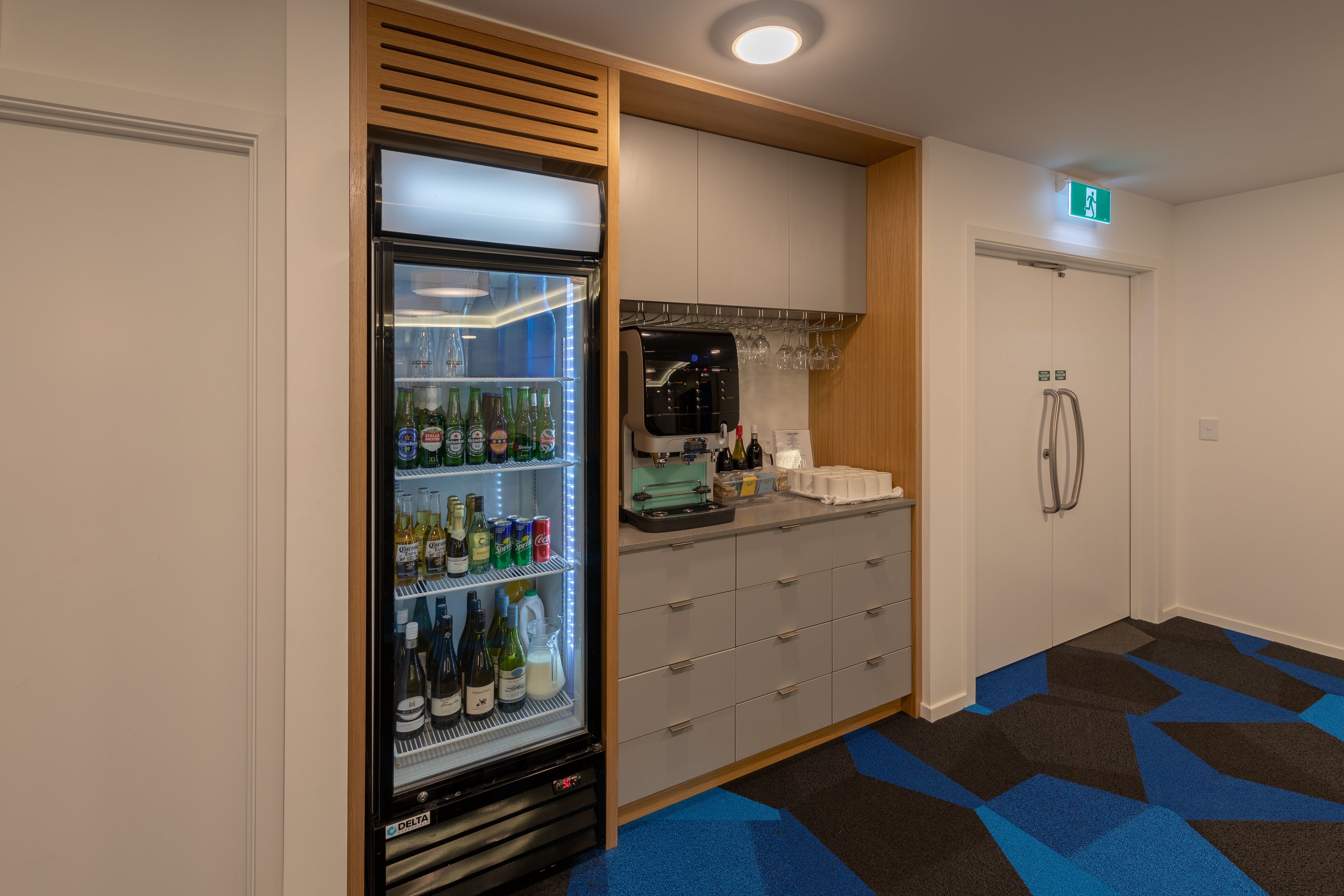 A compact hotel room with a minibar, a refrigerator stocked with beverages, a coffee machine, and a small bar area.