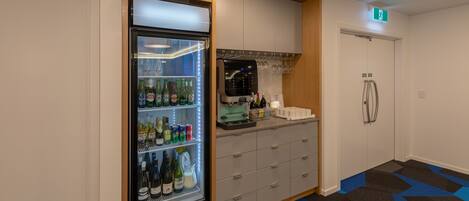 Una habitación de hotel compacta con minibar, refrigerador lleno de bebidas, máquina de café y una pequeña zona de bar.