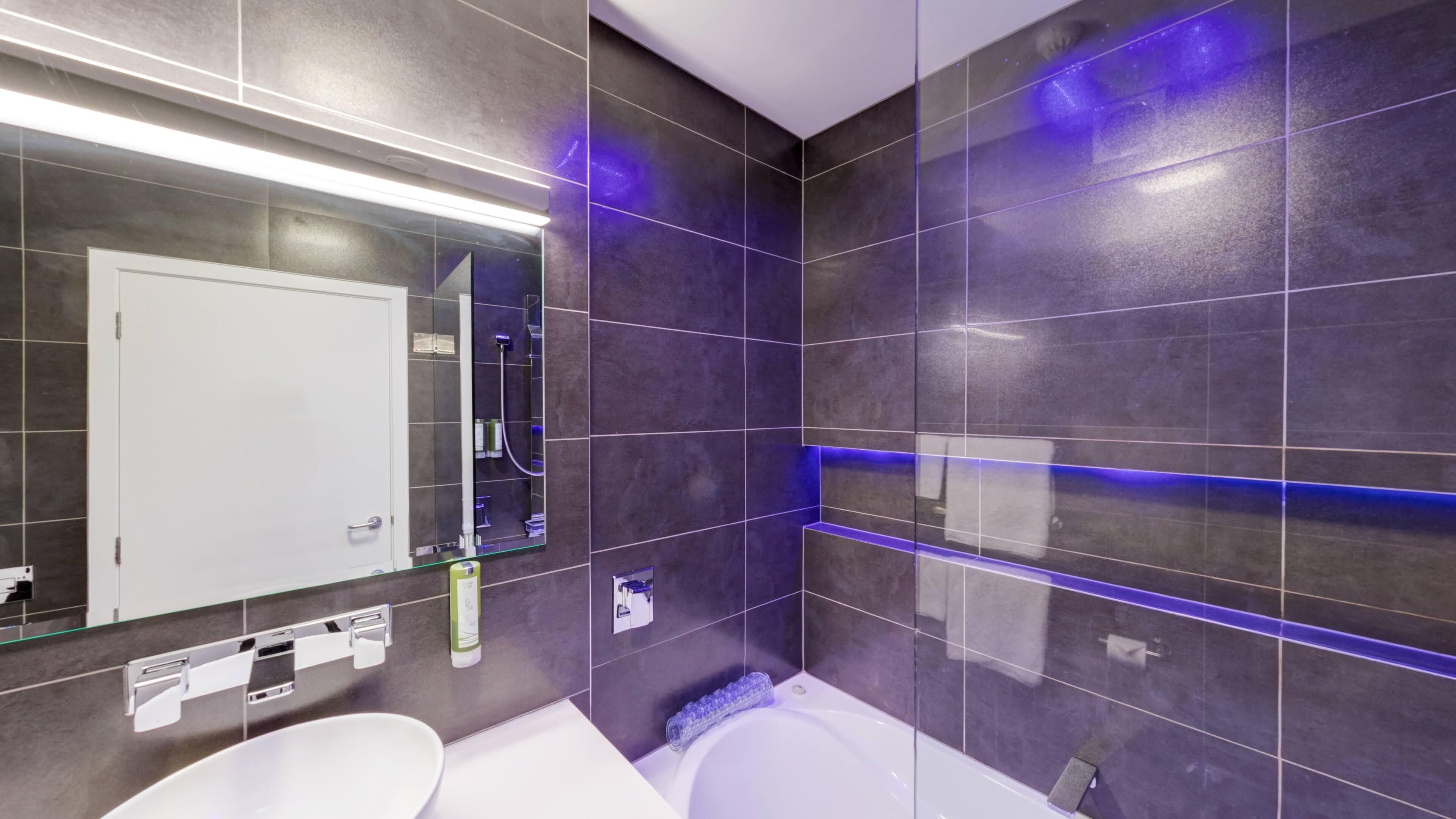 A modern bathroom with dark tiles, a white sink, a large mirror, and a bathtub.