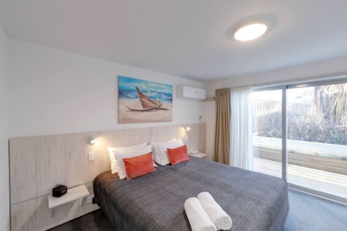 Ett modernt hotellrum med en stor säng, en tavla som föreställer en segelbåt, ett fönster med utsikt över träd och ett nattduksbord med en lampa.