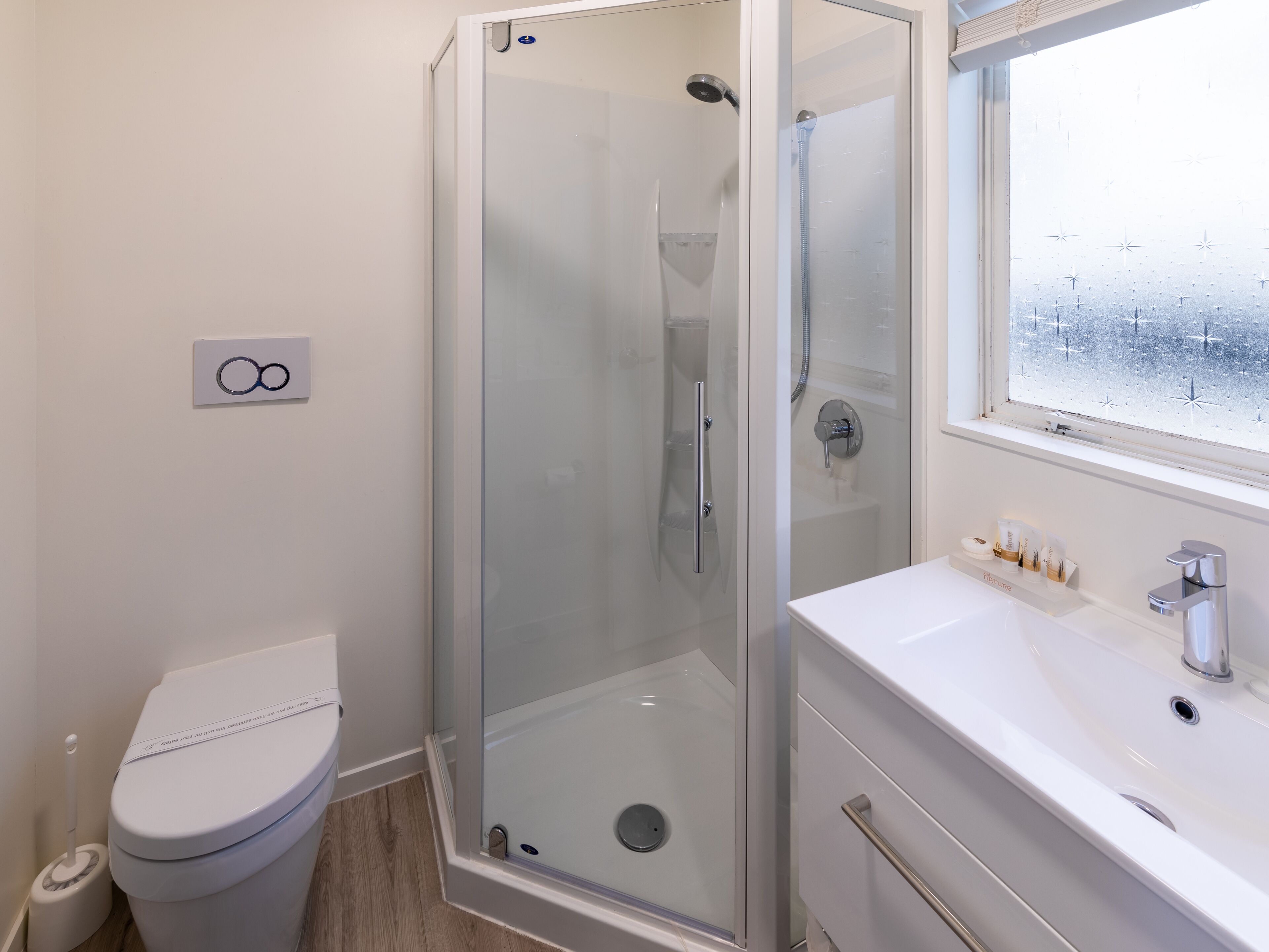 Un baño moderno con ducha de vidrio, inodoro blanco y lavamanos con artículos de tocador.
