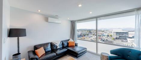 A modern living room with a black leather sofa, a blue armchair, and a view of the city through large windows.