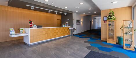 A reception area with a wooden reception desk, a blue carpet, and a potted plant.