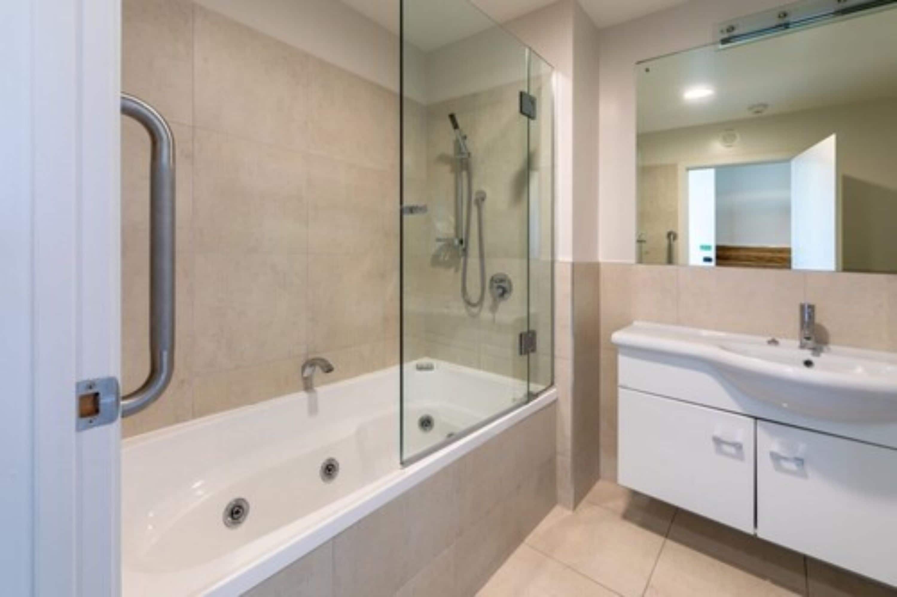 A modern bathroom with a glass-enclosed shower, a white bathtub, and a sink with a mirror above it.