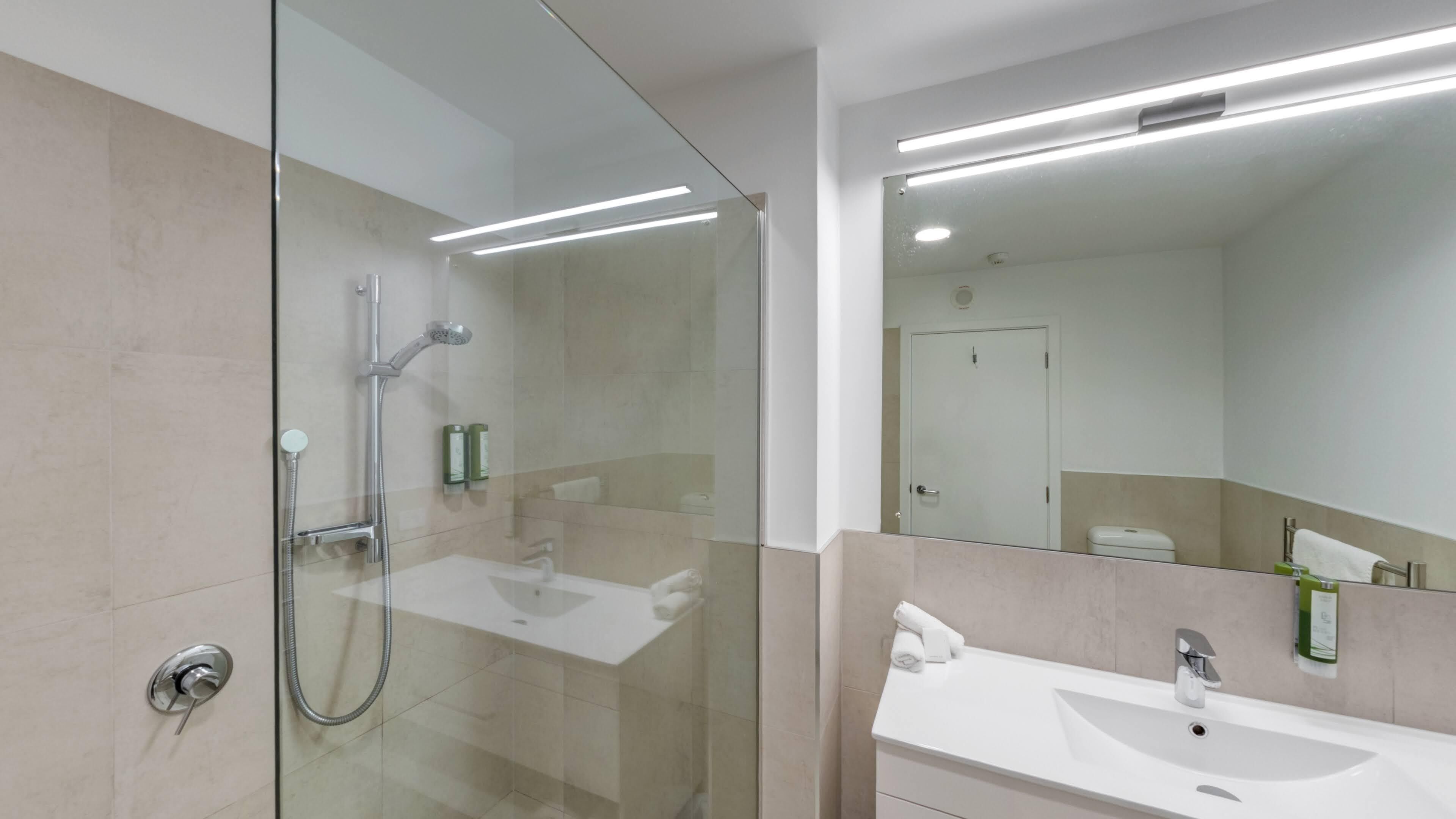A modern bathroom with a glass-enclosed shower, a white sink, and a large mirror above the sink.