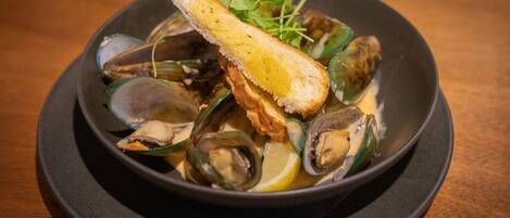 Un plato de mejillones con una rebanada de pan y limón sobre un plato negro.