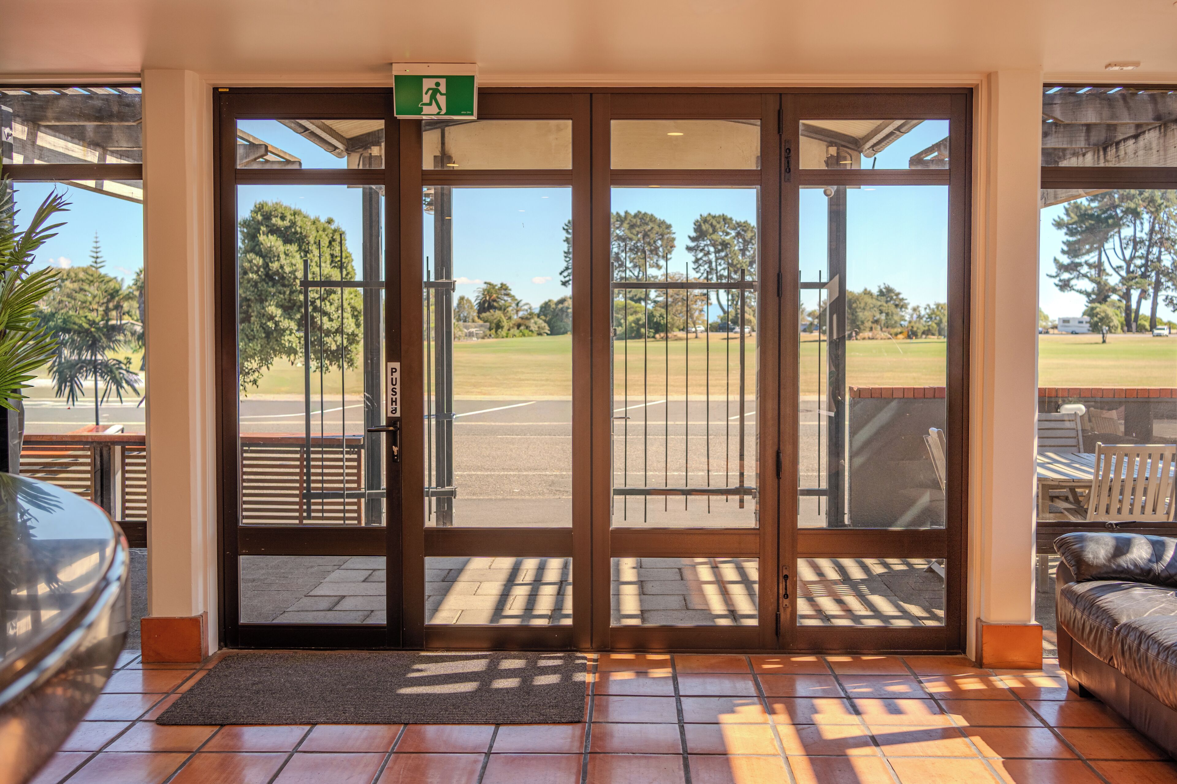 A hotel entrance with a glass door, a view of a golf course, and a patio area with outdoor furniture.