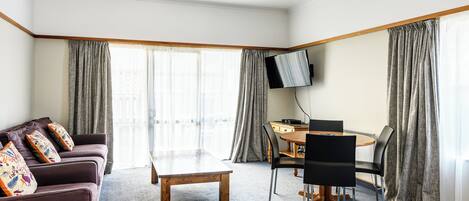 A living room with a sofa, a coffee table, a TV mounted on the wall, and a dining area with a table and chairs.