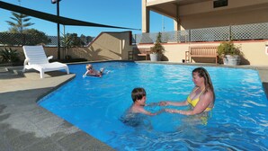 A swimming pool area with lounge chairs and a bench, surrounded by a covered patio. - The Beachcomber Hotel (Nelson)