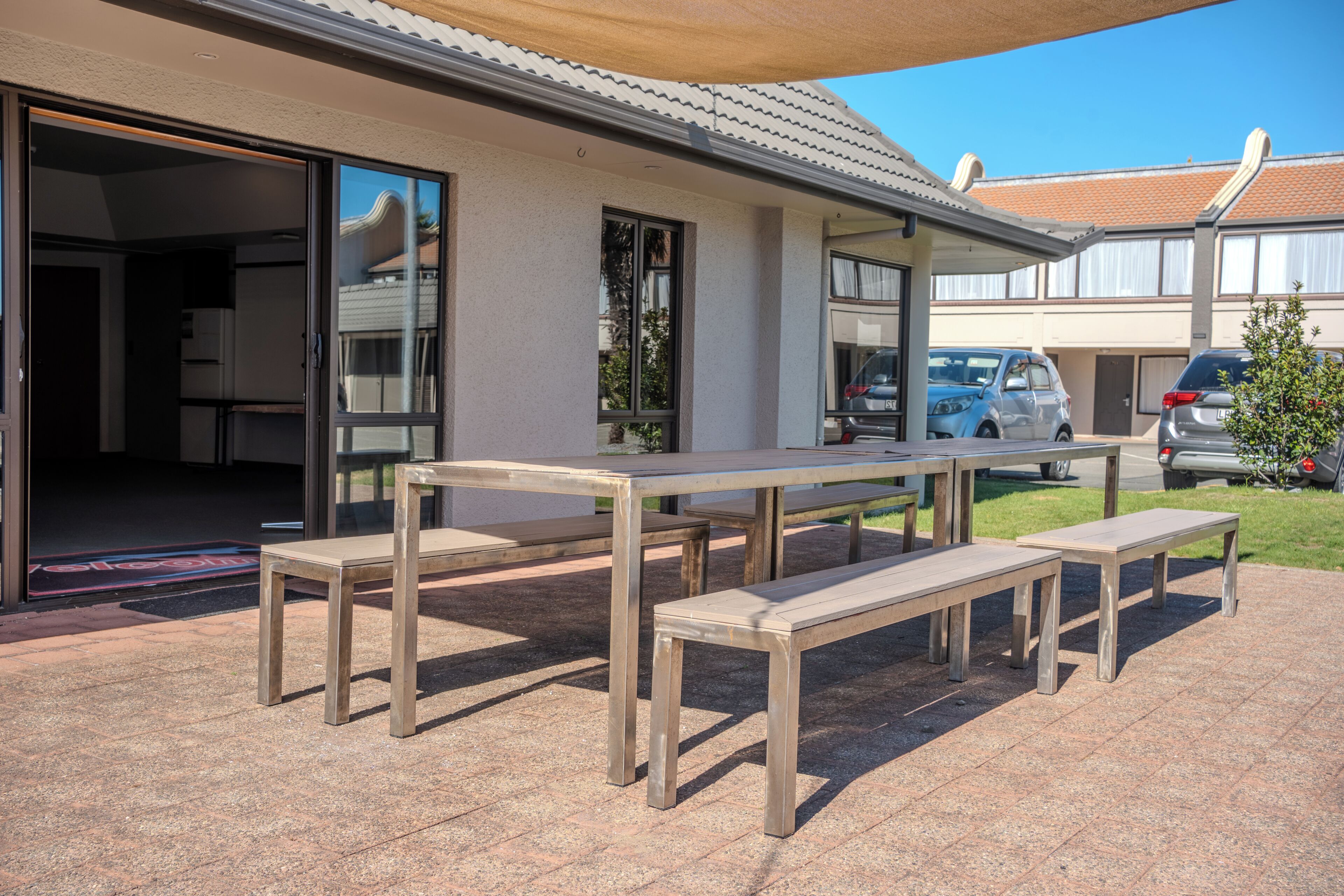 An outdoor patio with a table and benches, a sliding glass door entrance, and parked cars in the background.