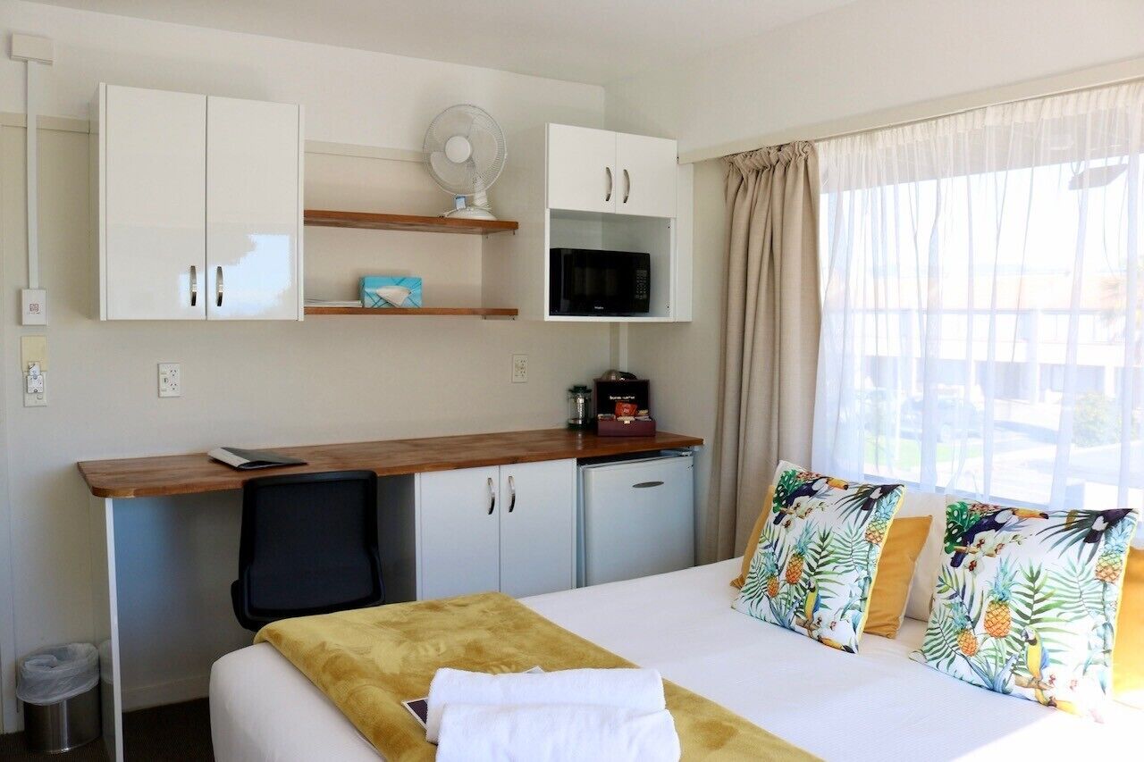Habitación de hotel con cama, escritorio con silla, microondas, ventilador y ventana con cortinas.
