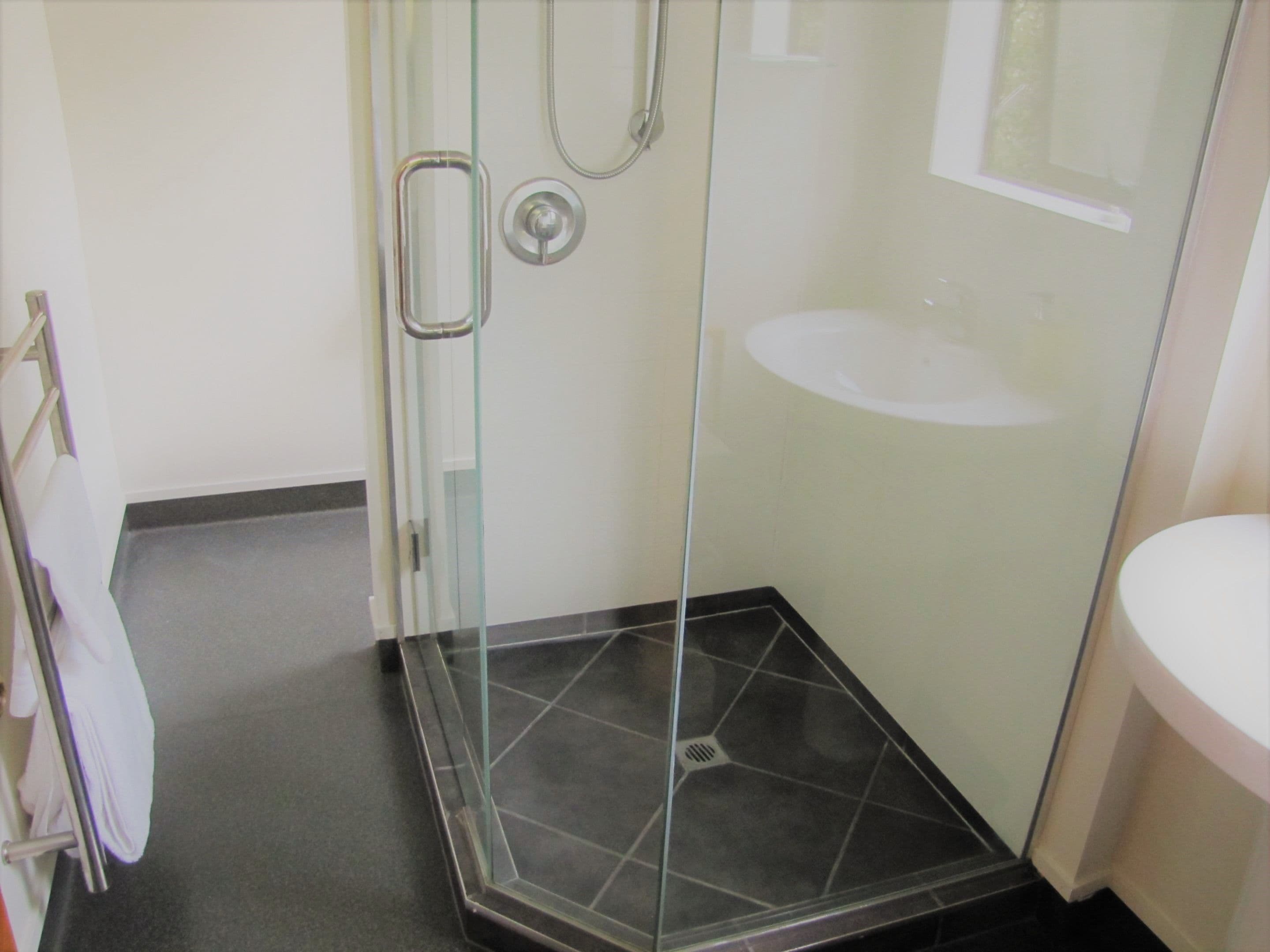 A bathroom with a glass shower enclosure, a white sink, and a towel rack.