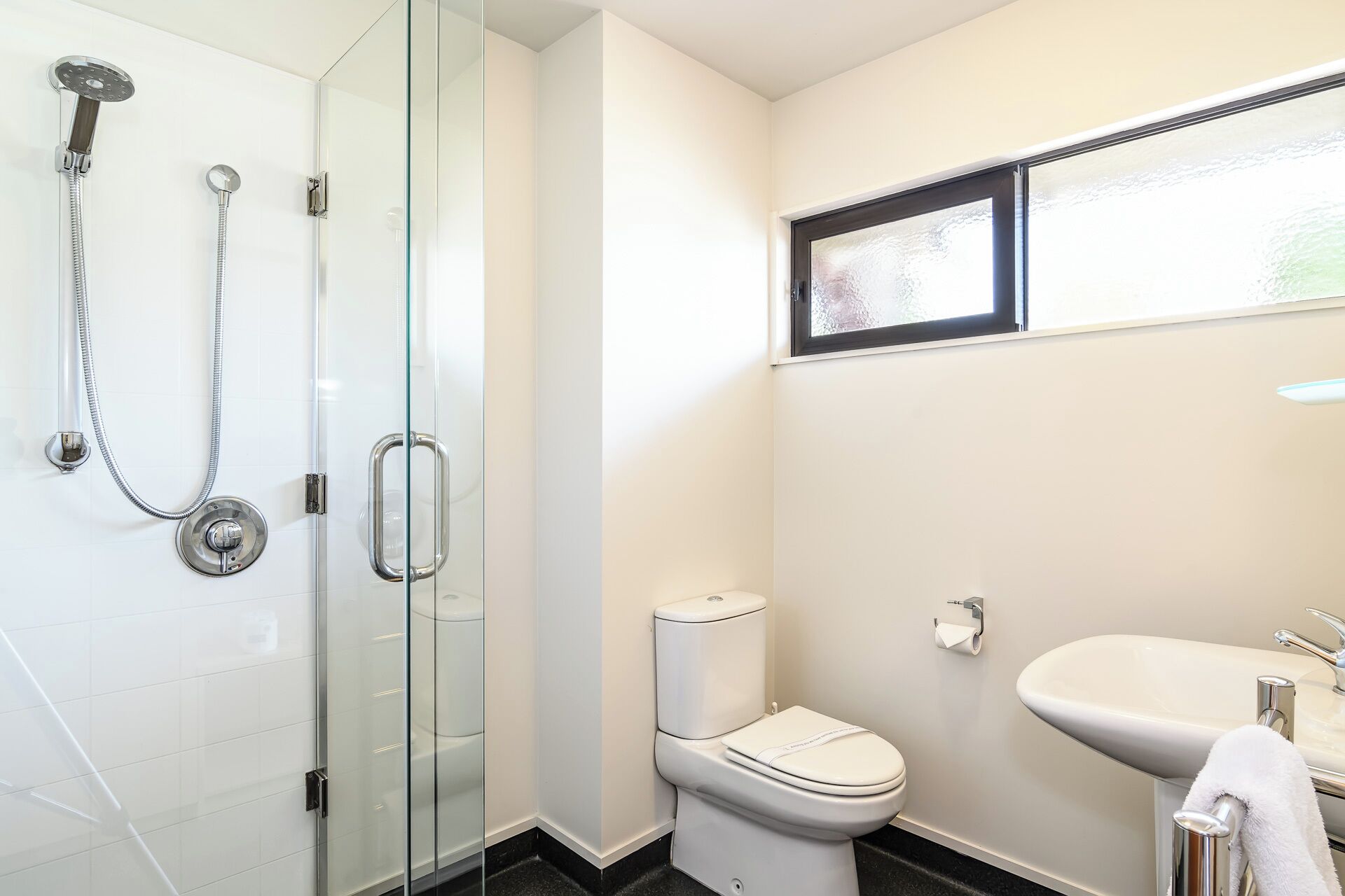A bathroom with a glass-enclosed shower, a toilet, and a sink.
