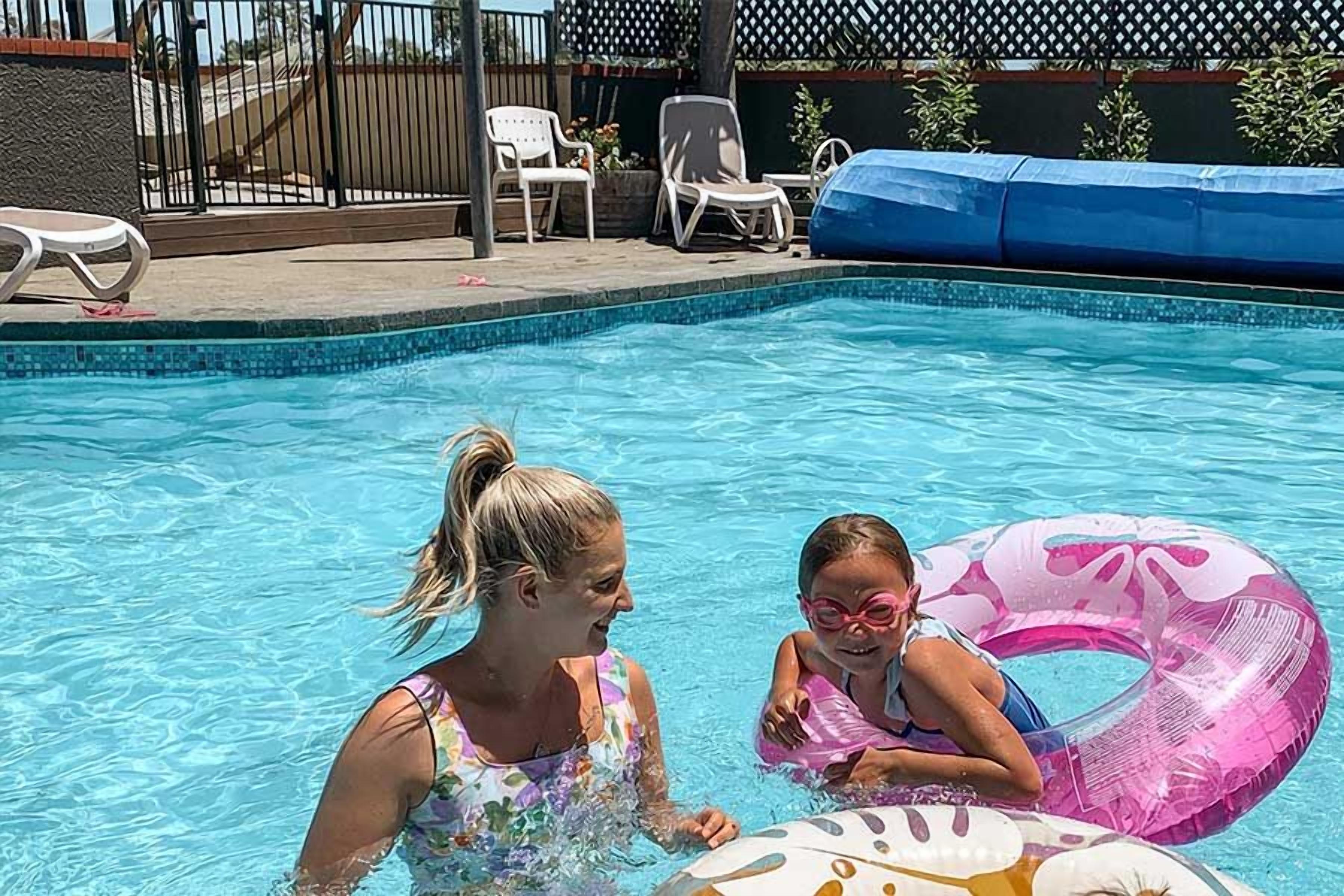 A swimming pool with a tiled edge, lounge chairs, and a fence in the background.