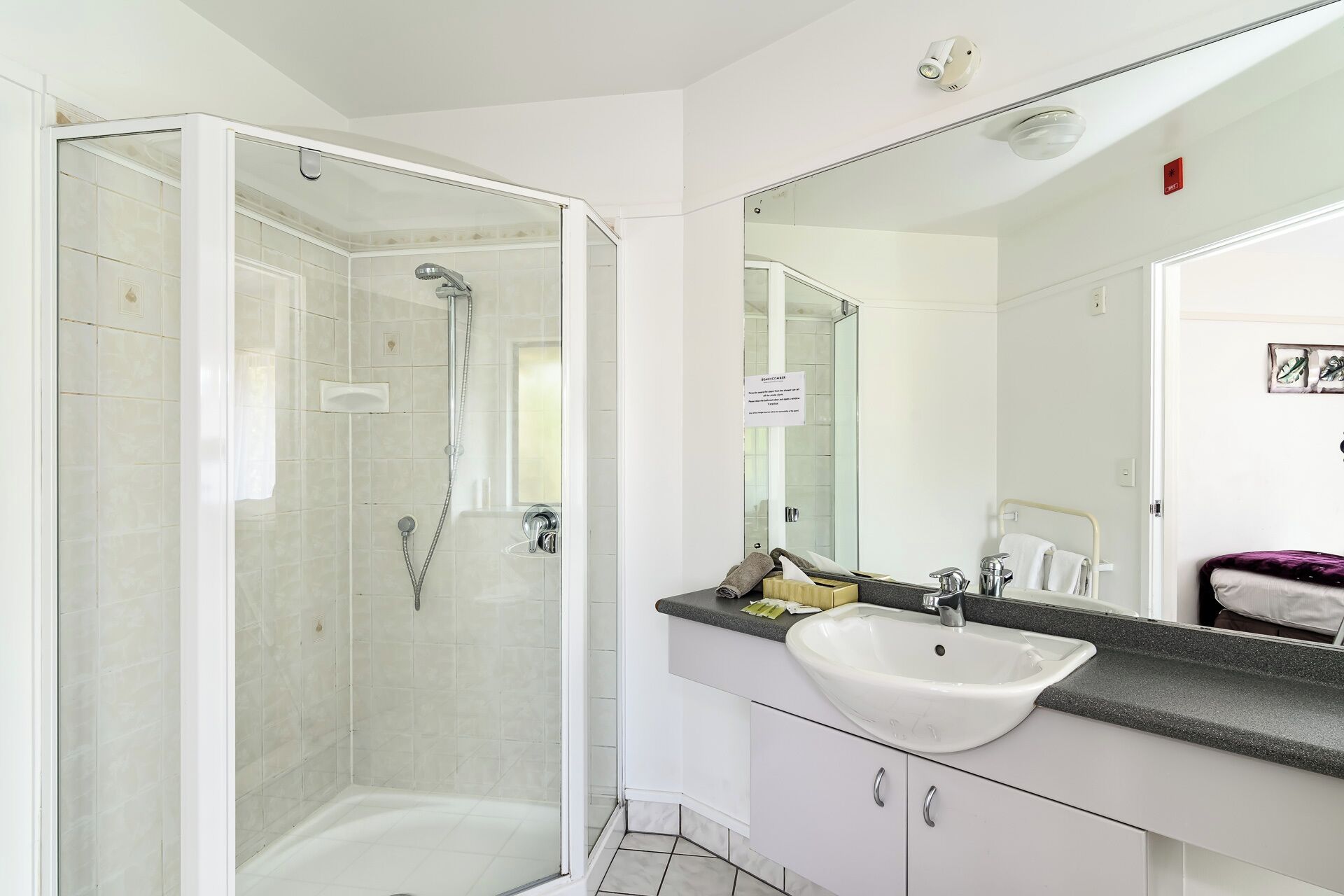Une salle de bain moderne avec une douche à parois de verre, un lavabo blanc et un grand miroir.