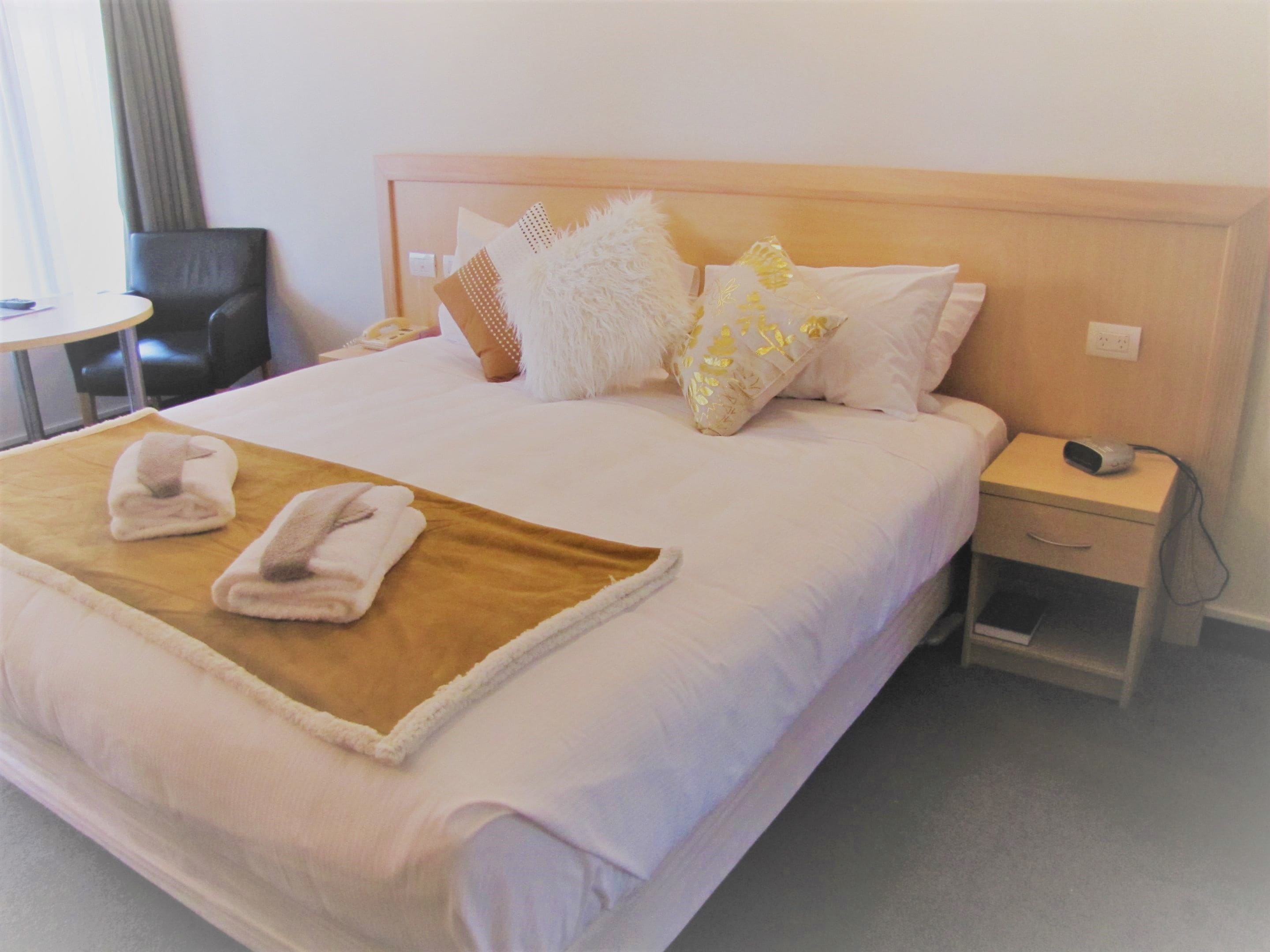 A hotel room with a large bed, a bedside table, a chair, and a small table.