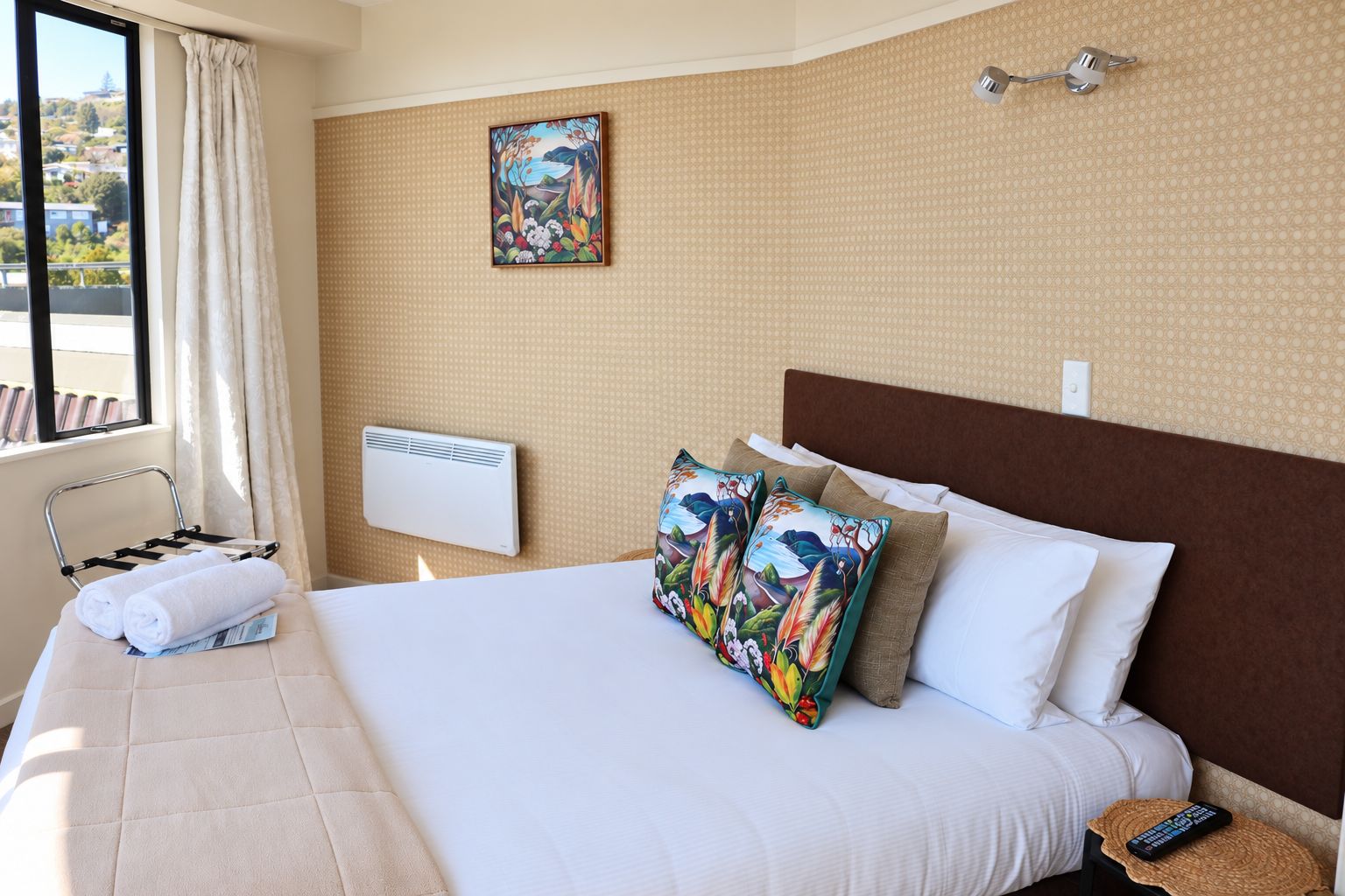 A hotel room with a large bed, a window with curtains, a painting on the wall, a radiator, and a towel rack with towels.