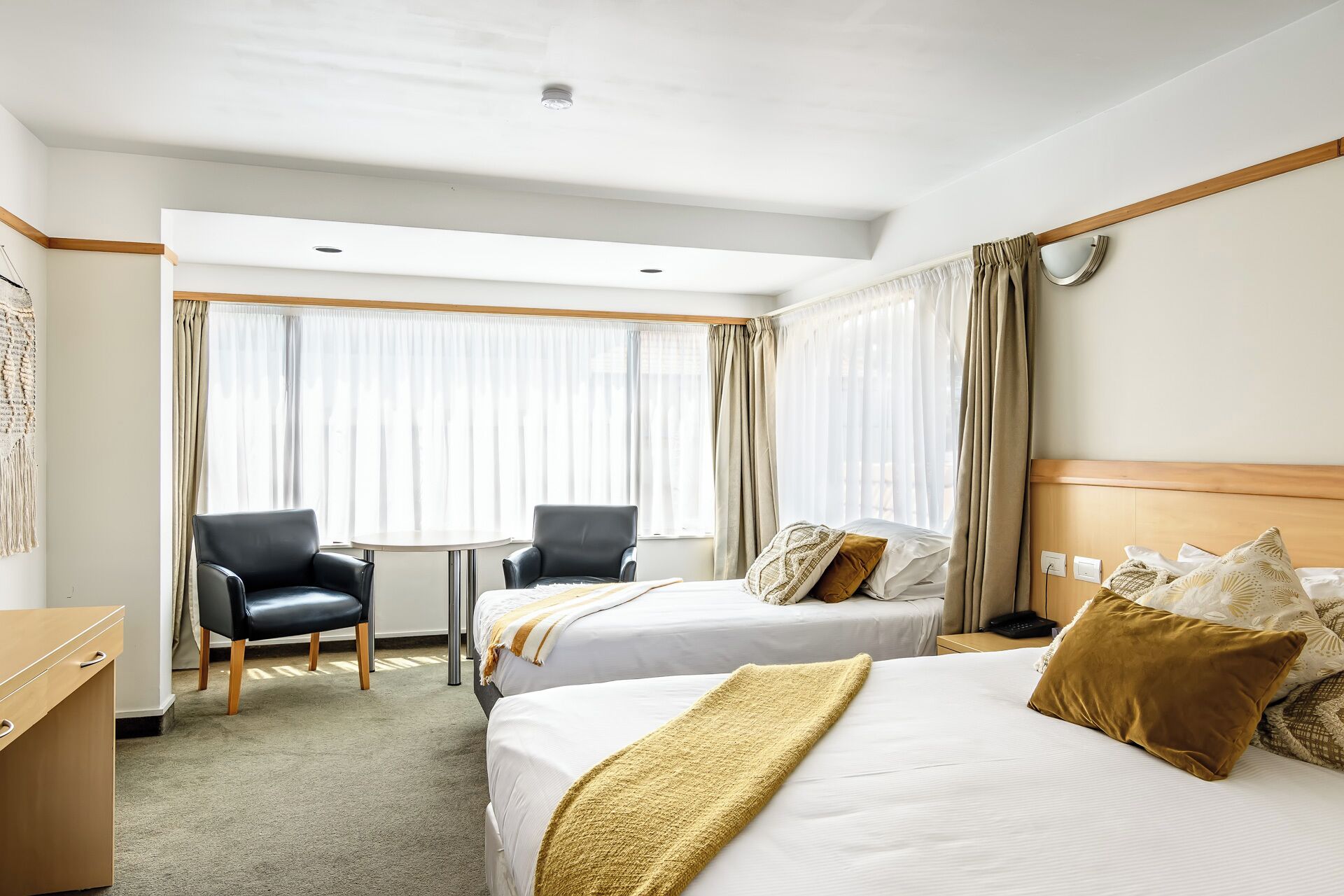 A hotel room with two beds, a desk, a chair, and a small table.