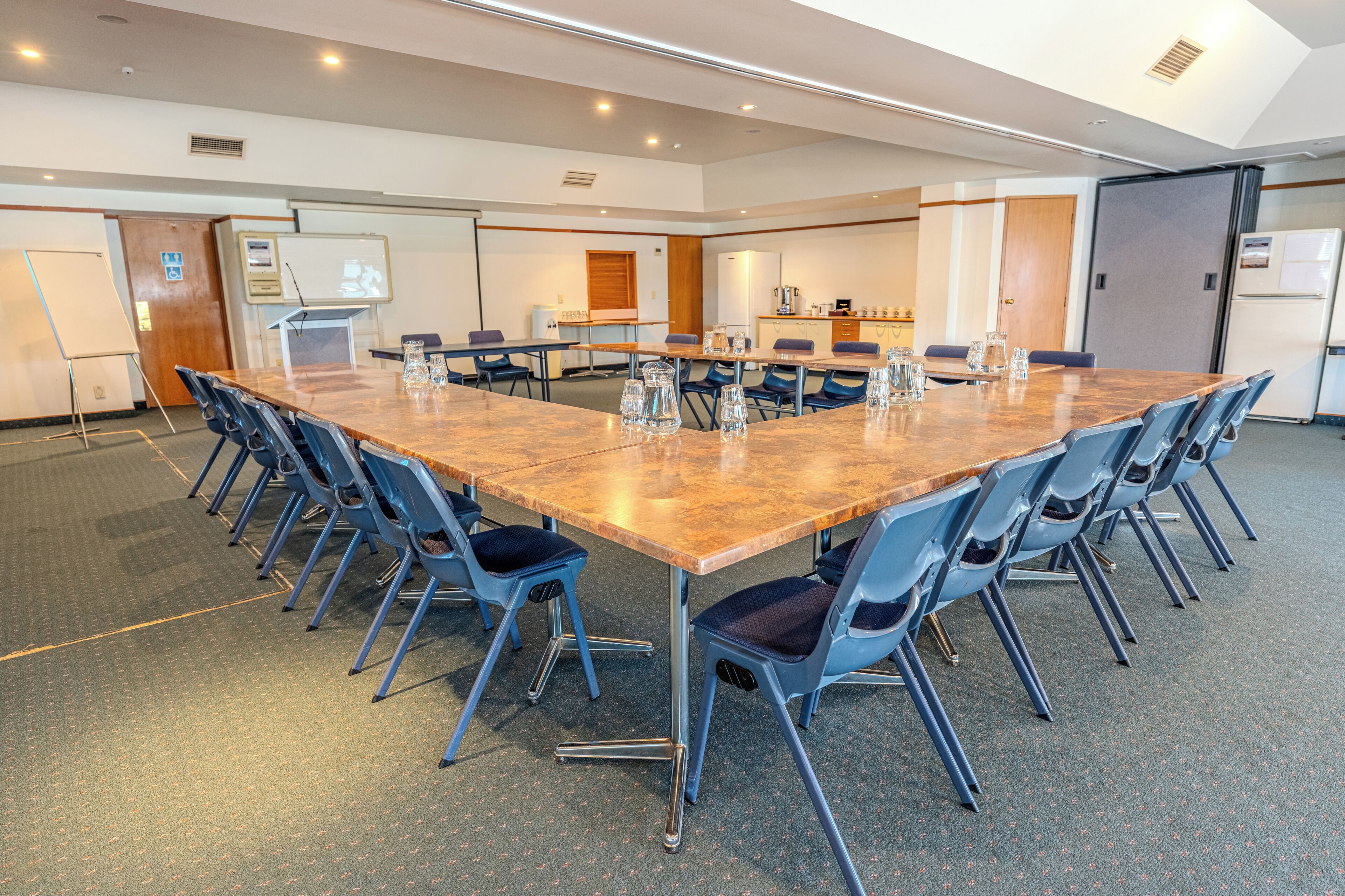 A conference room with a long table, blue chairs, a whiteboard, and a kitchenette area.