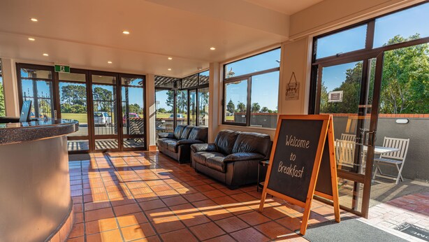 A reception area with a counter, seating, and a sign welcoming guests to breakfast. - The Beachcomber Hotel (Nelson)